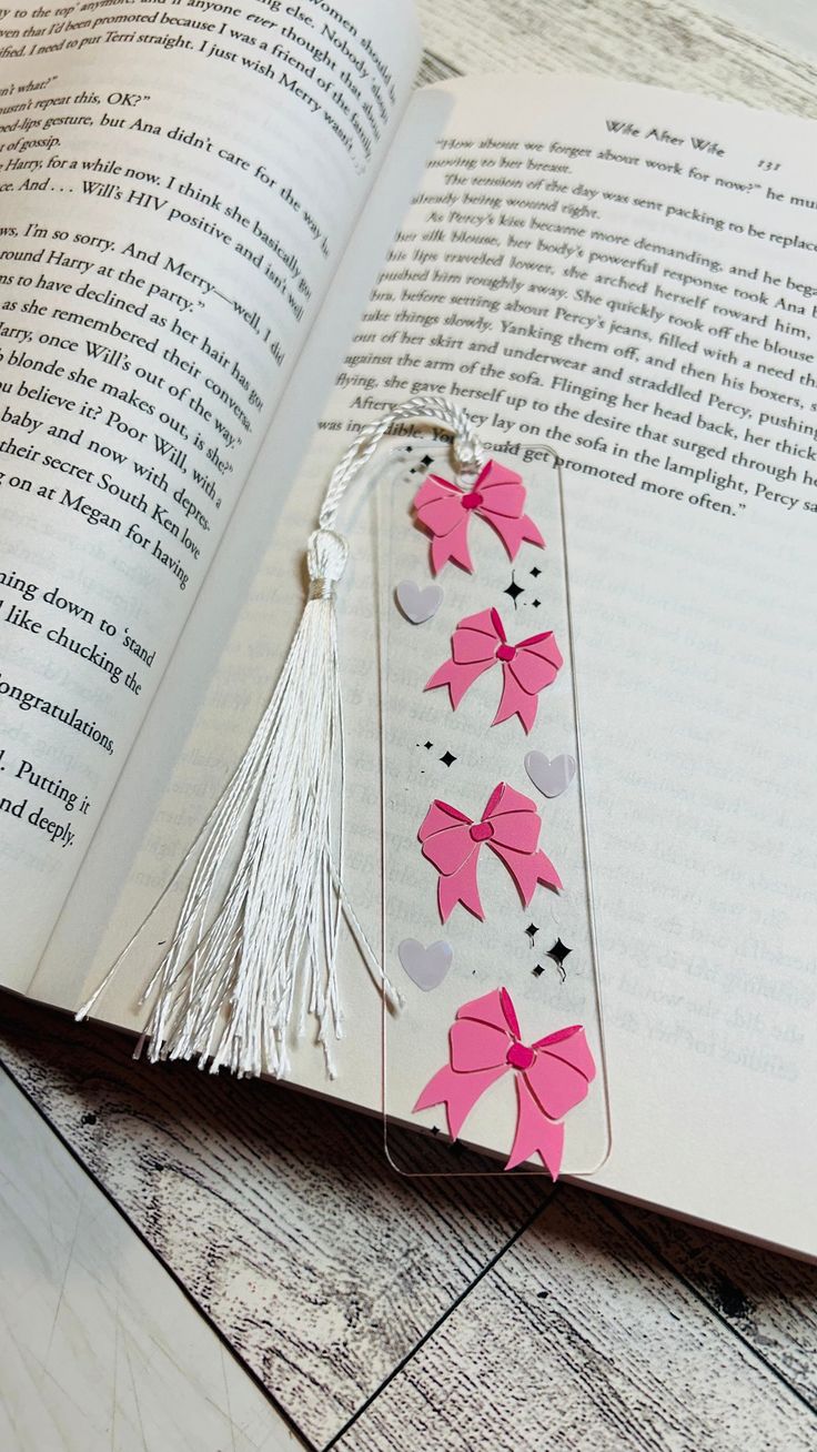 an open book with pink bows and tassels on the pages, next to a white string