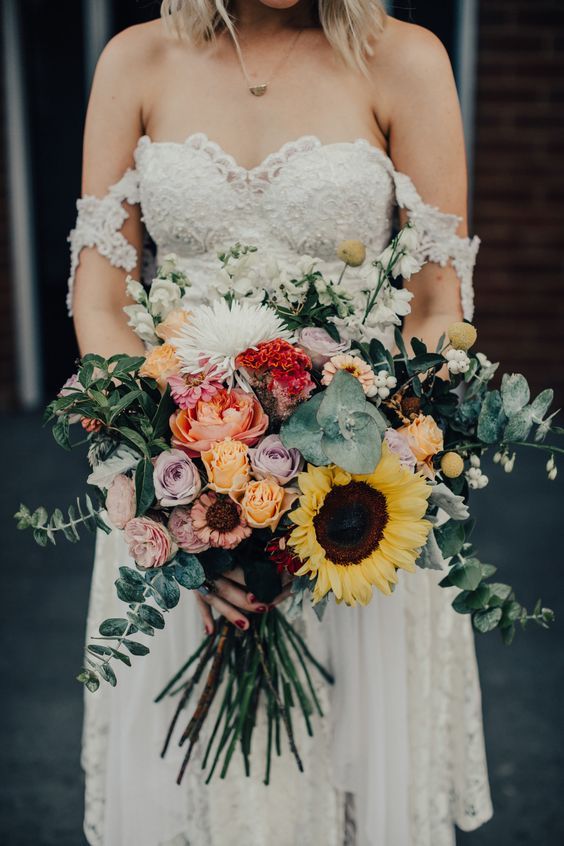 a woman in a white dress holding a bouquet of sunflowers and greenery