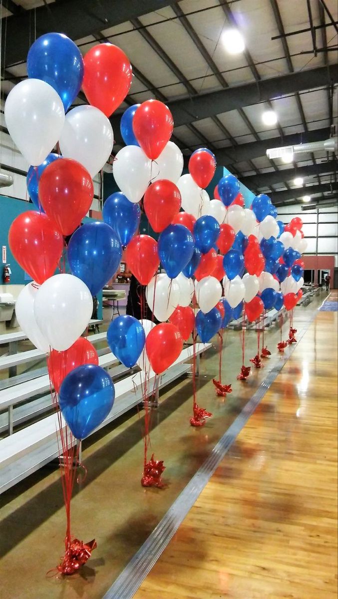 red, white and blue balloons are lined up on the floor in an empty gym