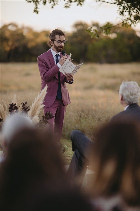 a man in a purple suit is holding a paper and standing next to an audience