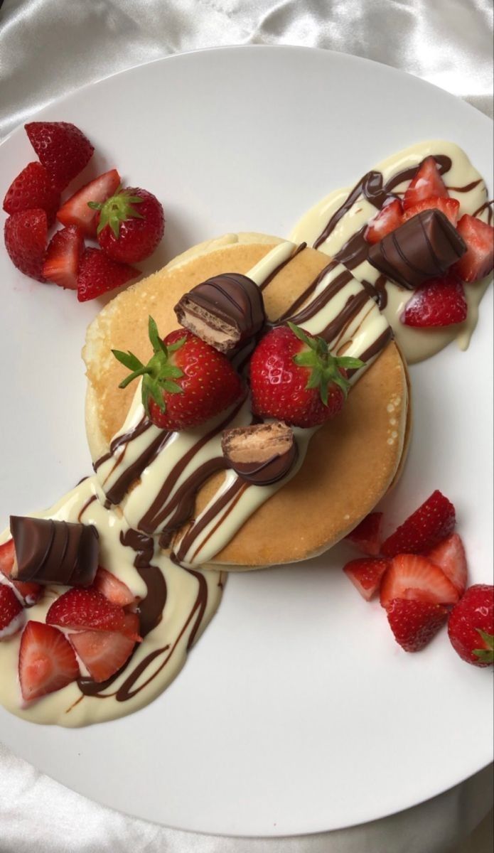 a white plate topped with pancakes covered in chocolate and strawberries