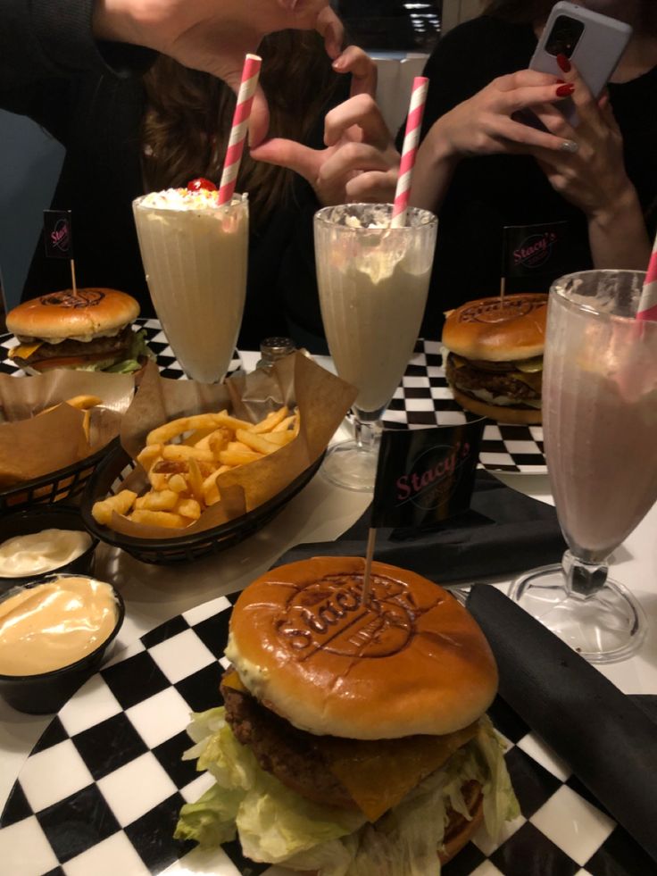 a table topped with hamburgers and fries next to two drinks on top of it