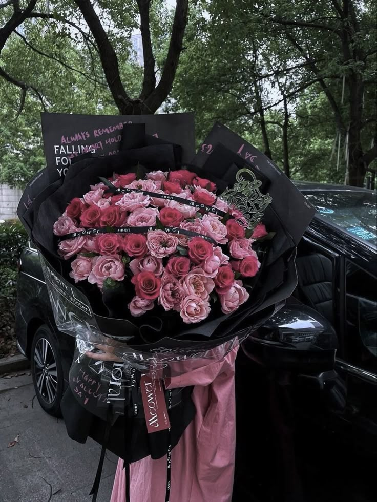 a bouquet of pink roses is being held by a woman in front of a car