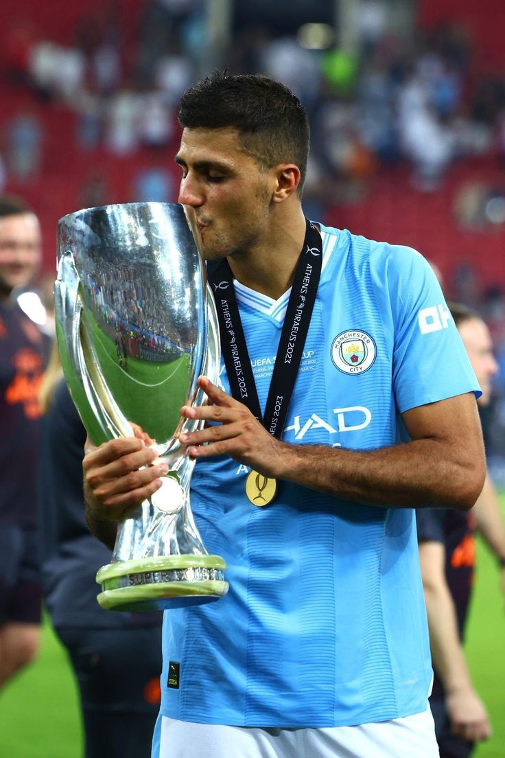 a man holding a trophy in front of his face and looking at the camera while standing on a soccer field