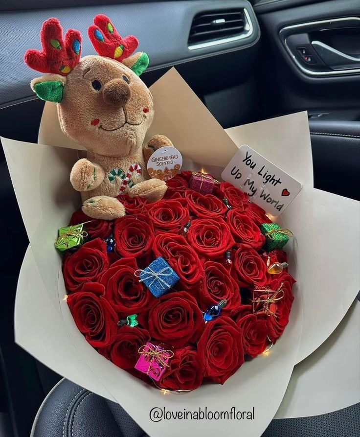 a teddy bear sitting on top of a bouquet of red roses in the passenger seat