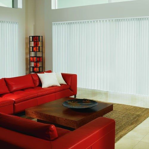 a living room with red couches and white vertical blinds on the windows behind them