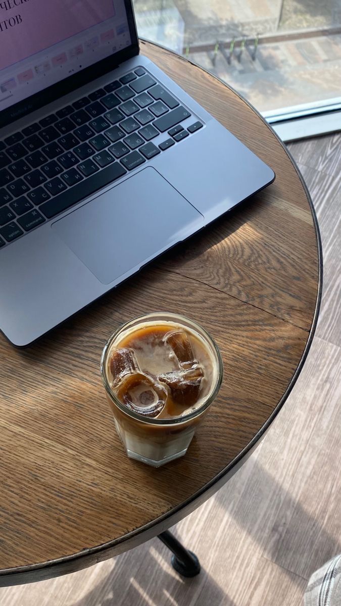 a laptop computer sitting on top of a wooden table next to a cup of coffee