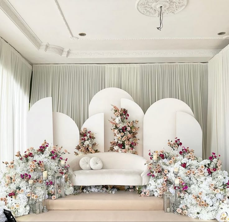 a white couch sitting on top of a stage covered in flowers and greenery next to a wall