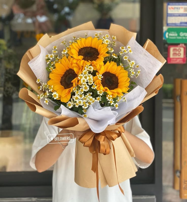 a woman holding a bouquet of sunflowers in front of a storefront window