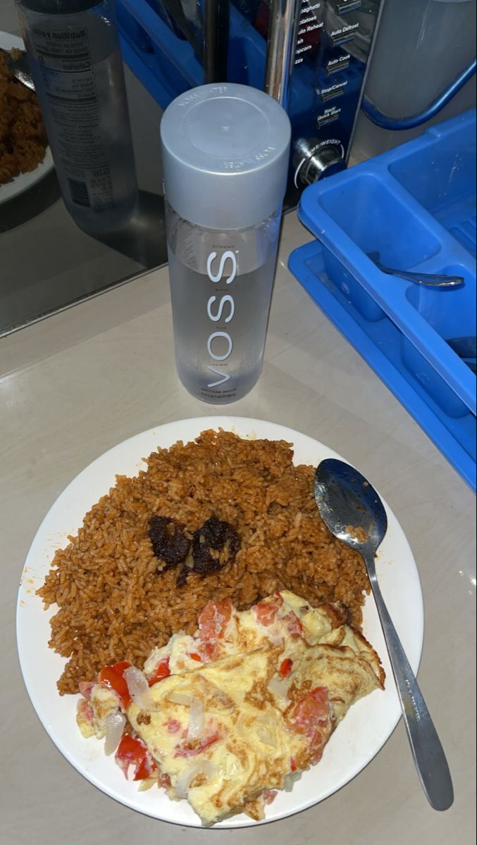 a white plate topped with rice, meat and veggies next to a water bottle