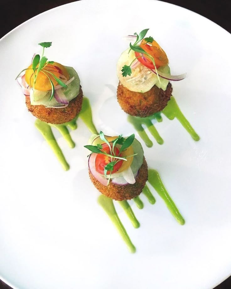 three small appetizers are on a white plate with green sauce and garnishes