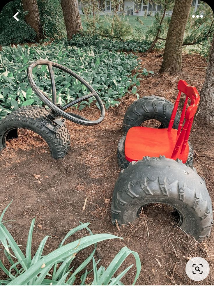 an orange chair sitting in the dirt next to two large tires and a metal object