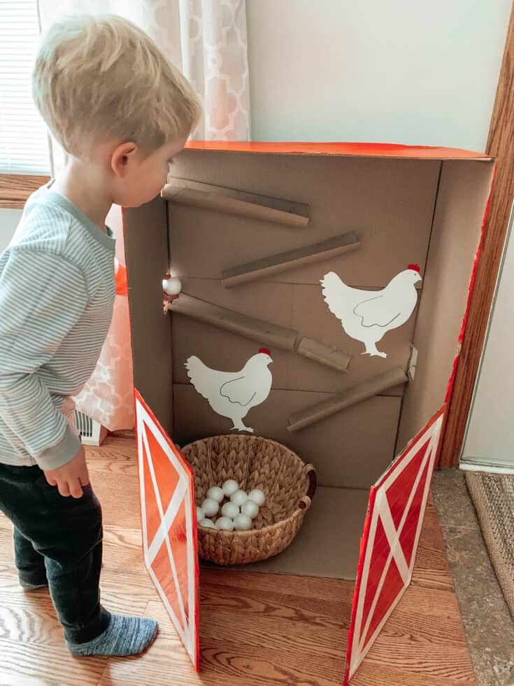 a little boy standing in front of a cardboard chicken coop