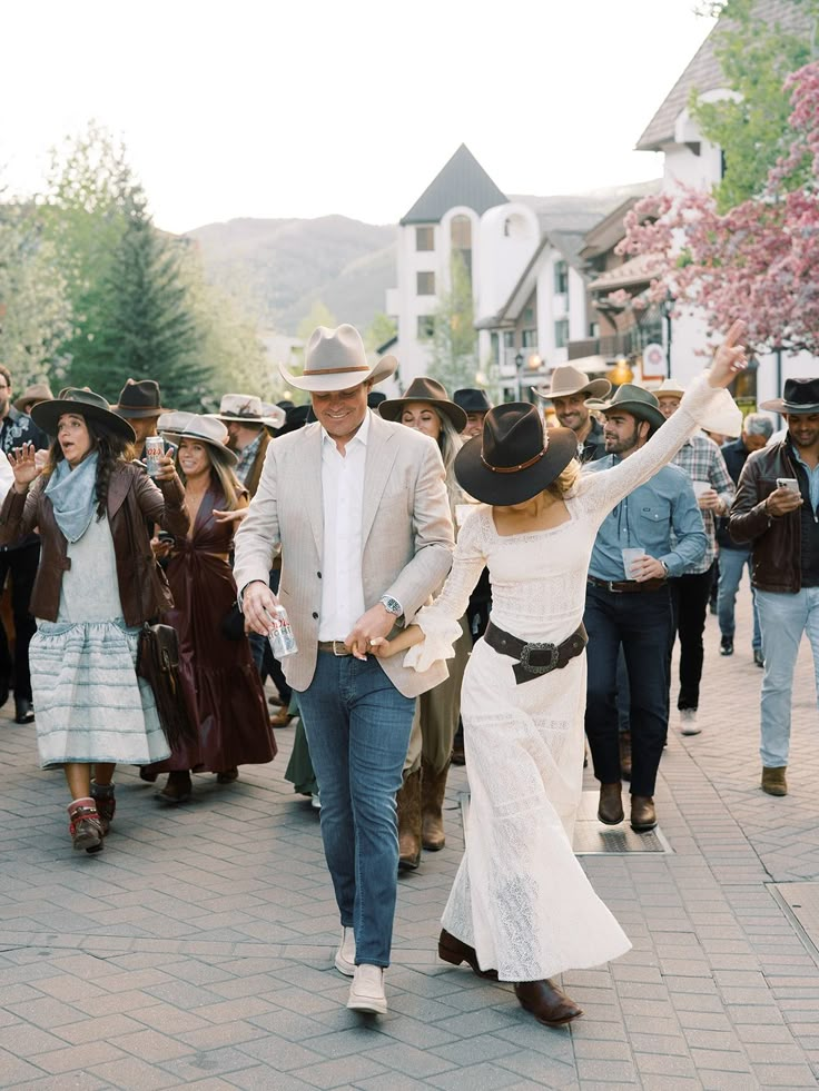 a man and woman walking down a street next to each other in cowboy hats on their heads