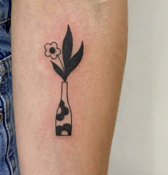 a black and white flower in a vase tattoo on the left arm by an unknown person