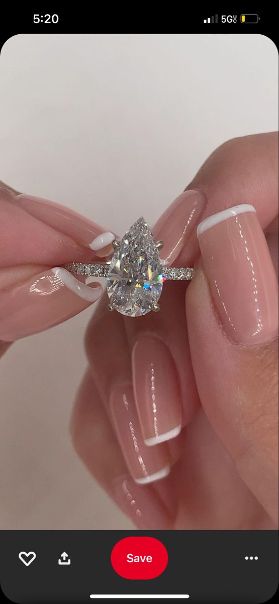 a woman's hand holding a diamond ring on her left hand, with white and pink manicured nails