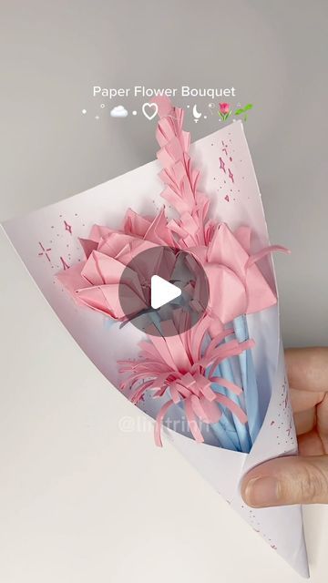 a hand holding a paper flower bouquet in it's left side, with pink flowers on the top