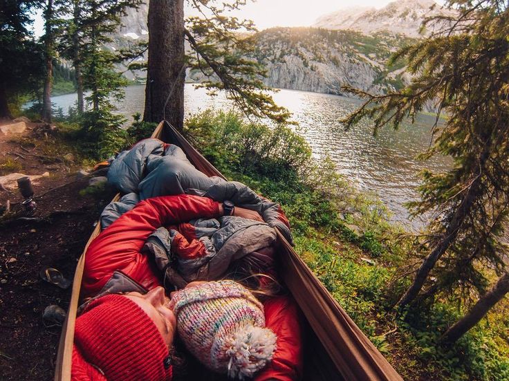 two people sleeping in a canoe on the side of a lake