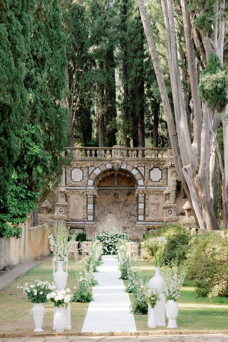 an outdoor ceremony setup with white flowers and greenery in vases on the ground