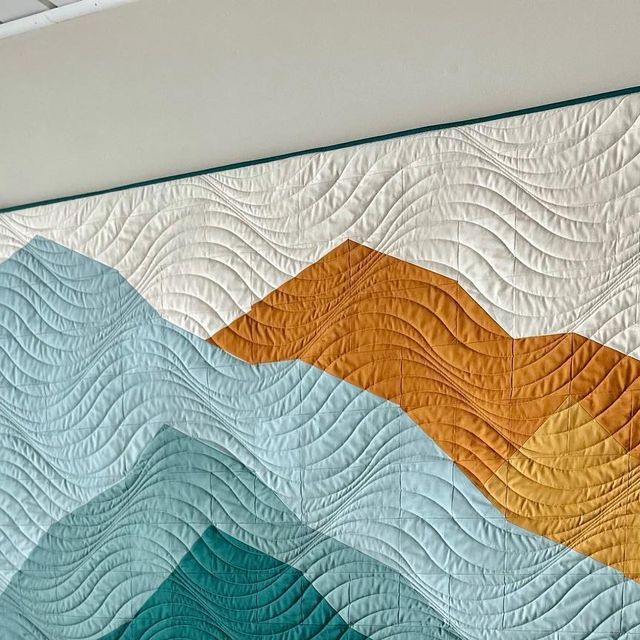 a quilted wall hanging on the side of a white building with blue, orange and yellow waves