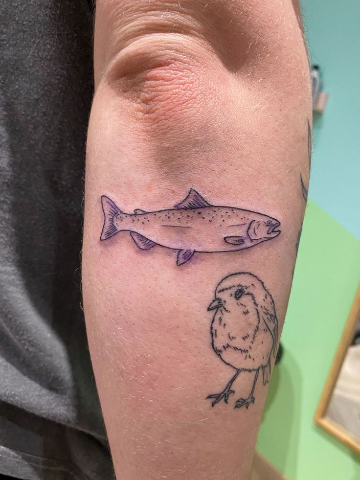 a man's arm with a fish tattoo on it and a bird sitting next to him