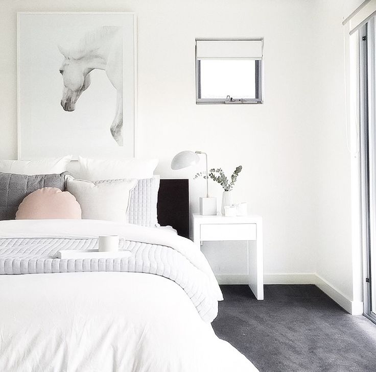 a white bedroom with a horse painting on the wall next to it's bed