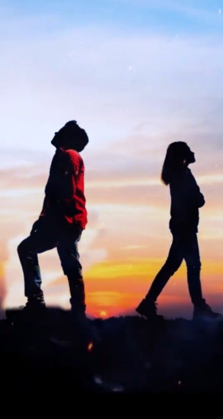 two people standing on top of a hill at sunset