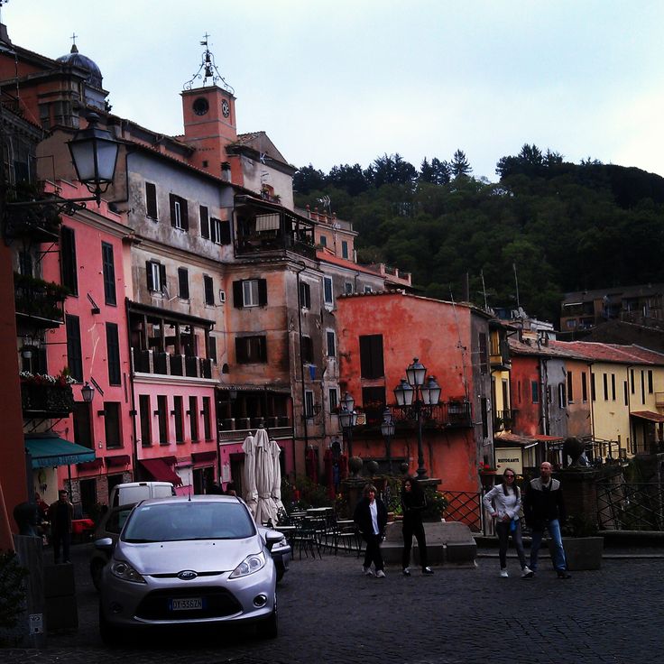 several people are standing in the middle of a cobblestone street lined with colorful buildings