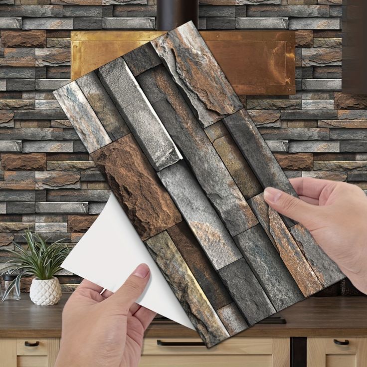 a person holding up some tile in front of a wall with stone and wood panels