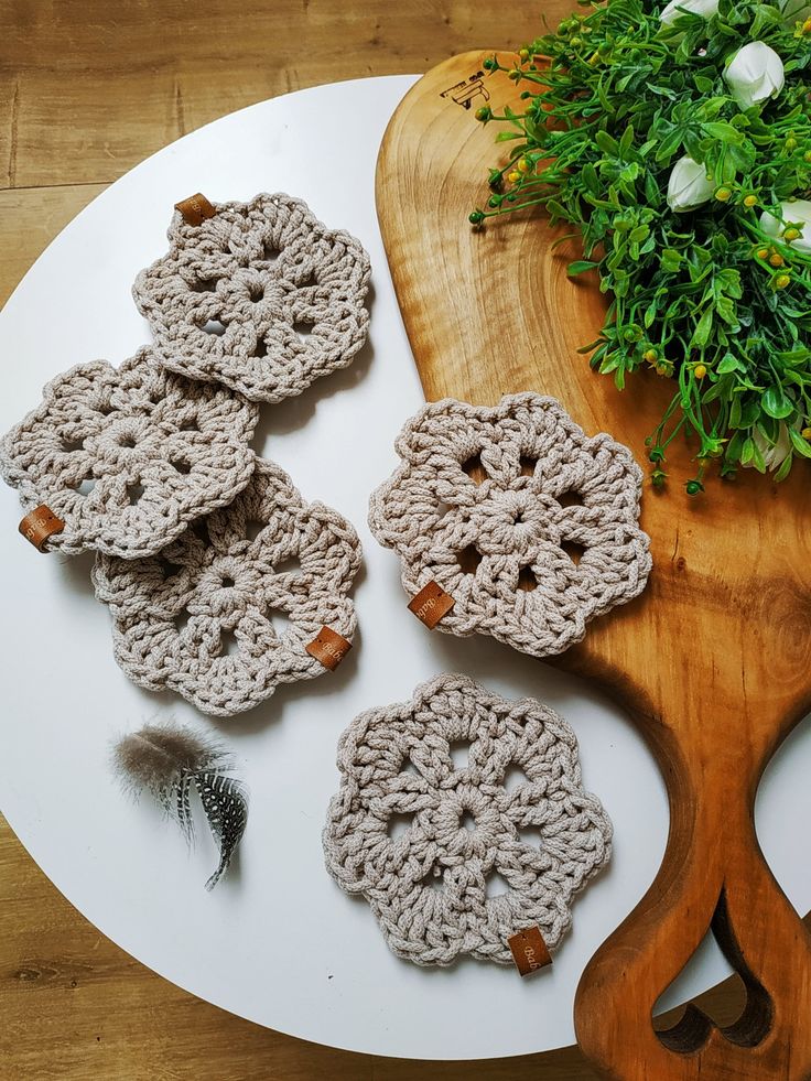 four crocheted coasters sitting on top of a white plate next to a plant