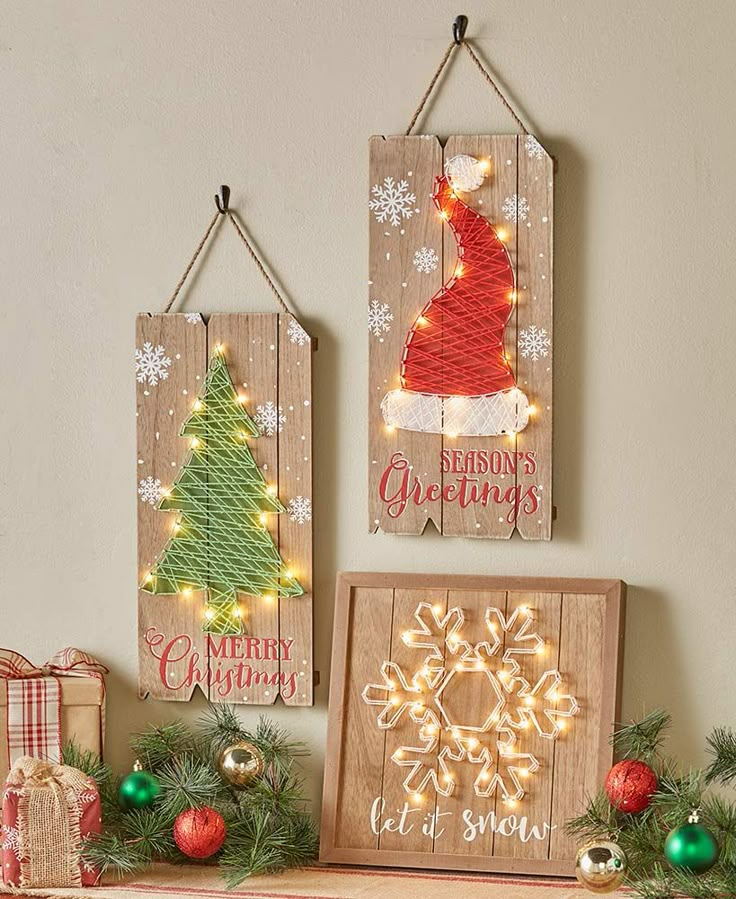 three wooden christmas signs hanging on a wall next to ornaments and presents in front of them