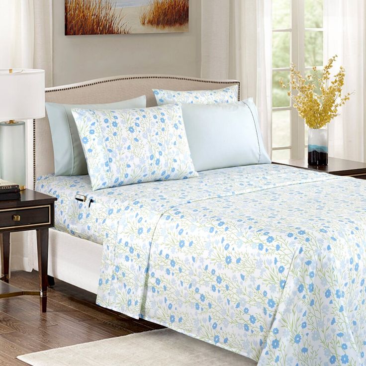 a bed with blue flowers on it in a bedroom next to a table and lamp