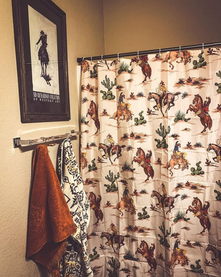 a shower curtain with horses on it next to a towel rack and a framed picture