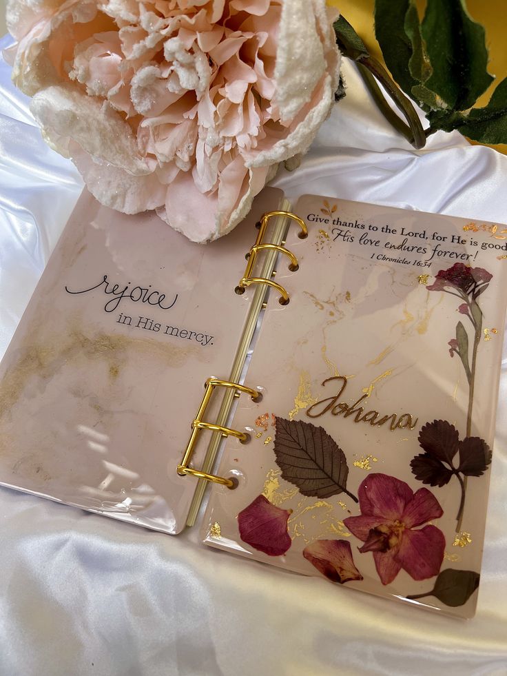 an open planner book sitting next to a pink flower