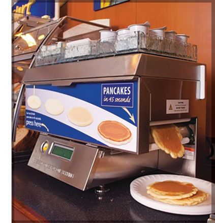 pancakes are being made in a machine at the breakfast counter with a plate of pancakes next to it