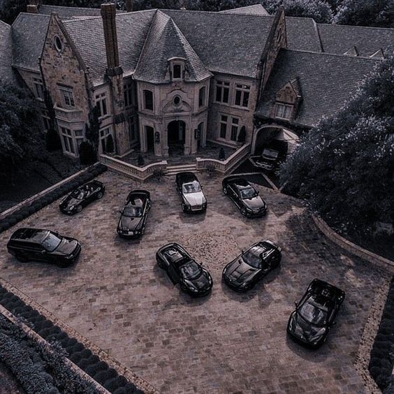 black and white photograph of cars parked in front of a large house