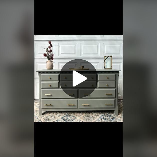 the dresser is painted gray with gold handles and drawers on each side, along with a vase filled with flowers