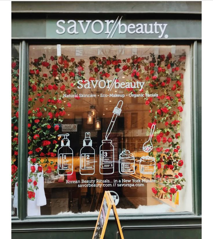 a store front window with flowers on the wall and an easel leaning against it