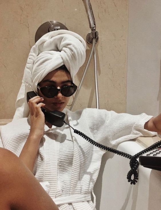 a woman with a towel on her head talking on the phone while sitting in a bathtub