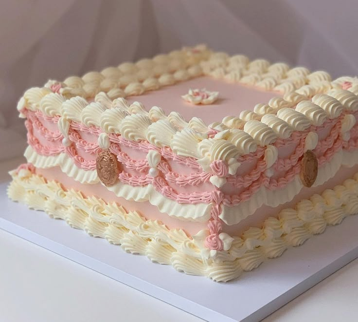 a square shaped cake with pink and white frosting on a white tableclothed surface