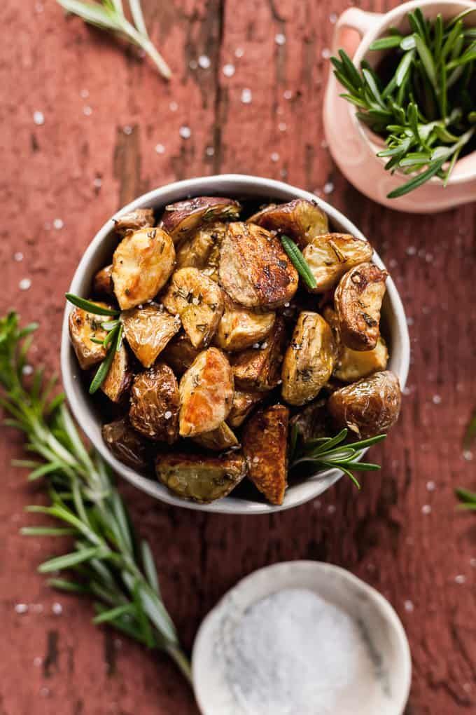 roasted potatoes in a bowl with rosemary sprigs on the side and two small dishes next to it