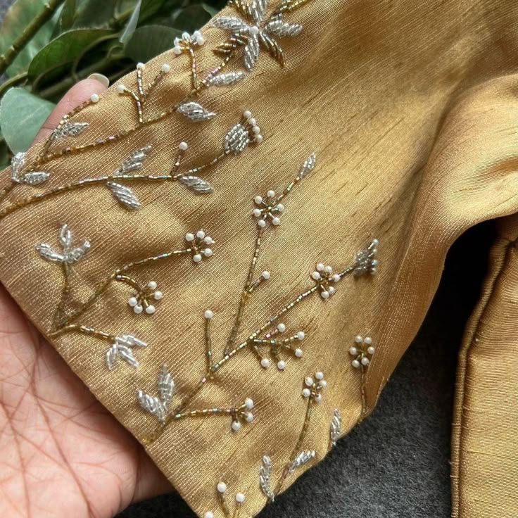 a hand holding a piece of cloth with beading on it and flowers in the background