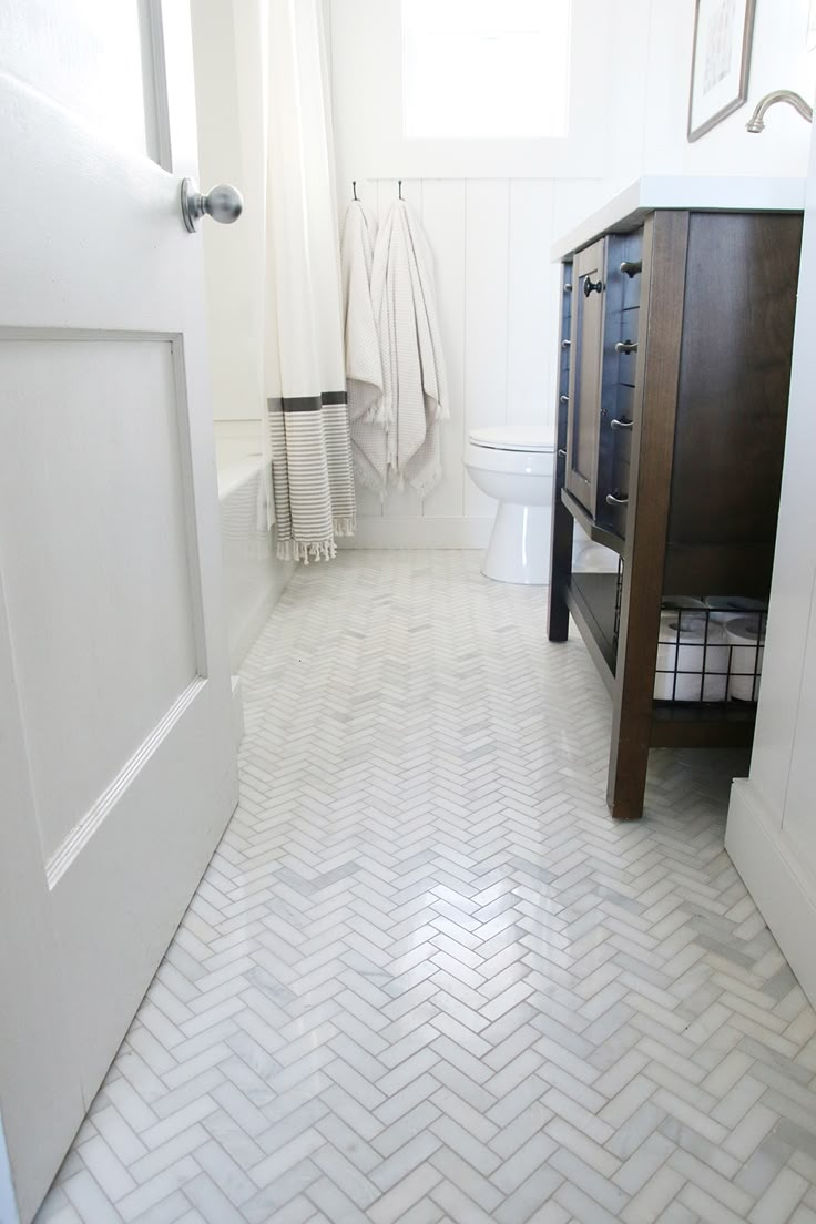 a white bathroom with herringbone tile flooring