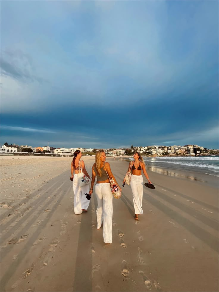 three women walking on the beach in white pants