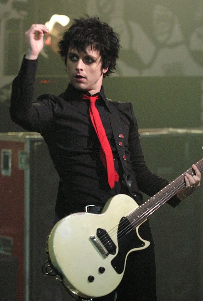 a man in black shirt and red tie holding up a white guitar with his right hand