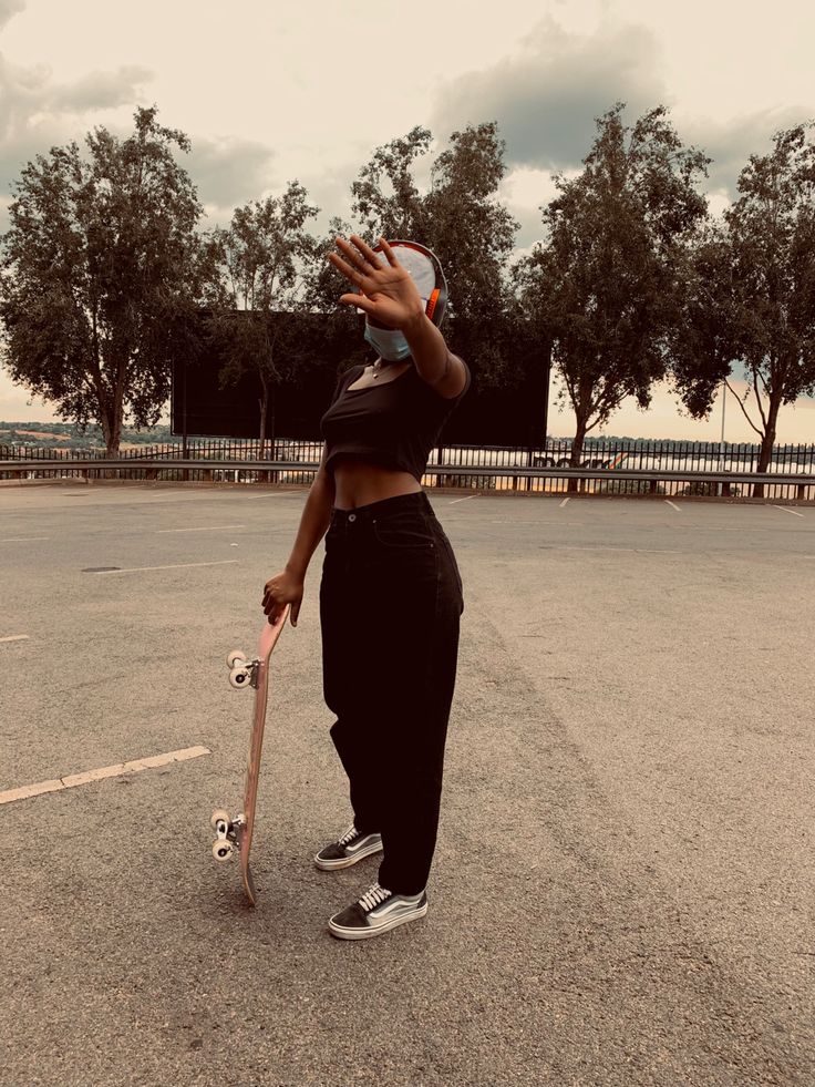 a woman holding a skateboard while standing in an empty parking lot