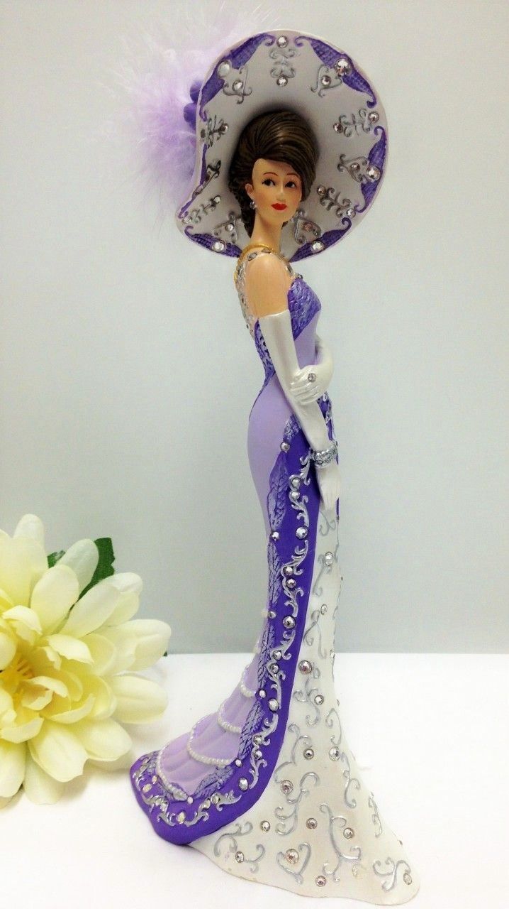 a figurine wearing a purple dress and hat with a flower in the foreground