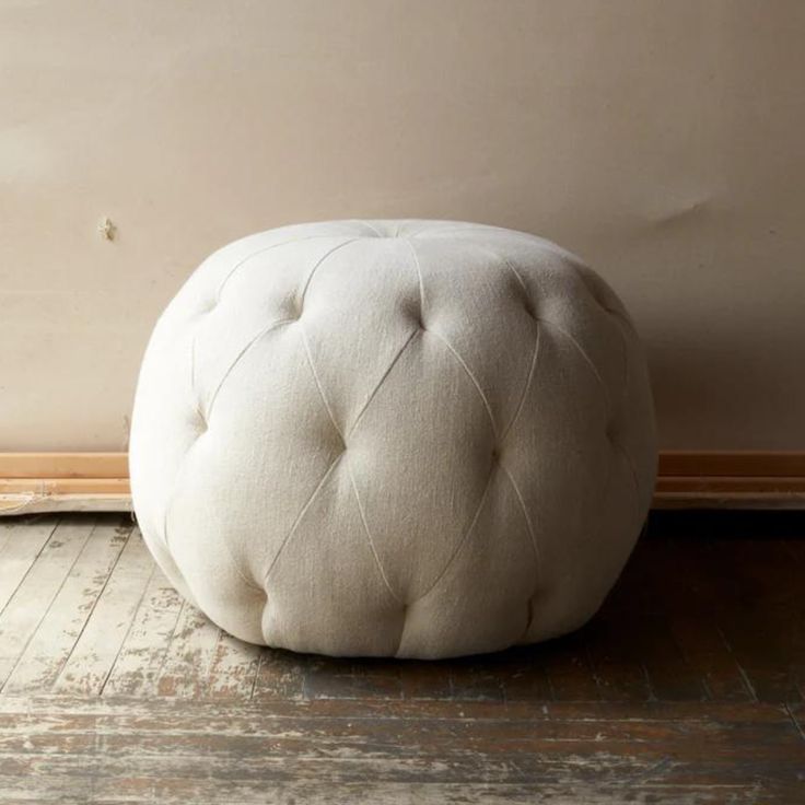 a white round foot stool sitting on top of a wooden floor next to a wall