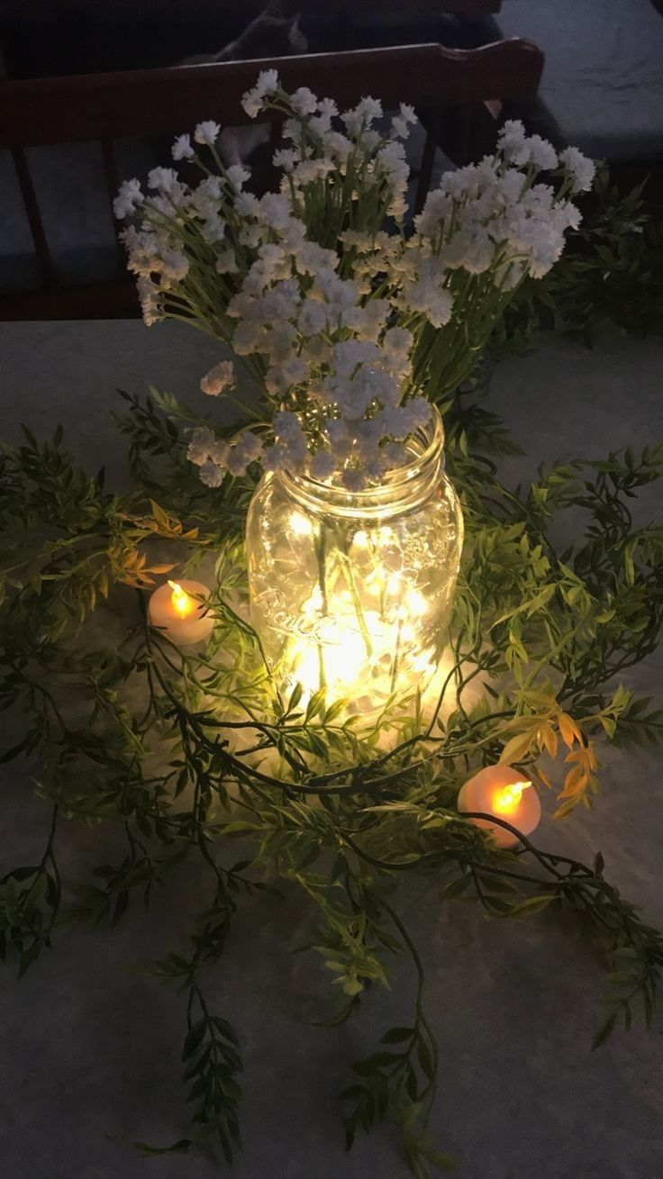 flowers and candles are lit in a mason jar on the ground, surrounded by greenery