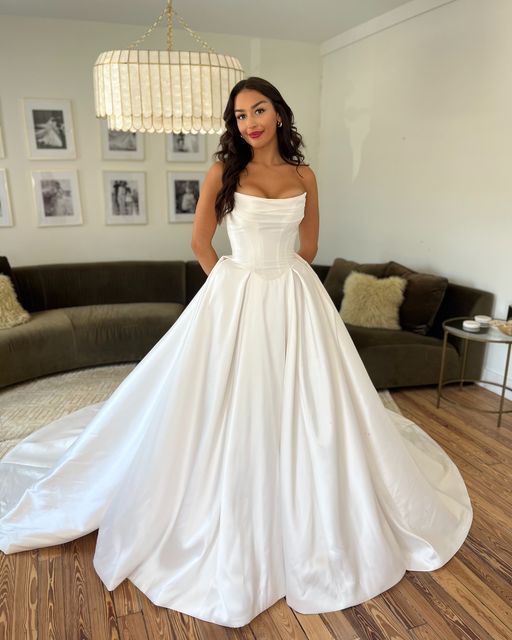 a woman in a white wedding dress standing next to a couch and looking at the camera